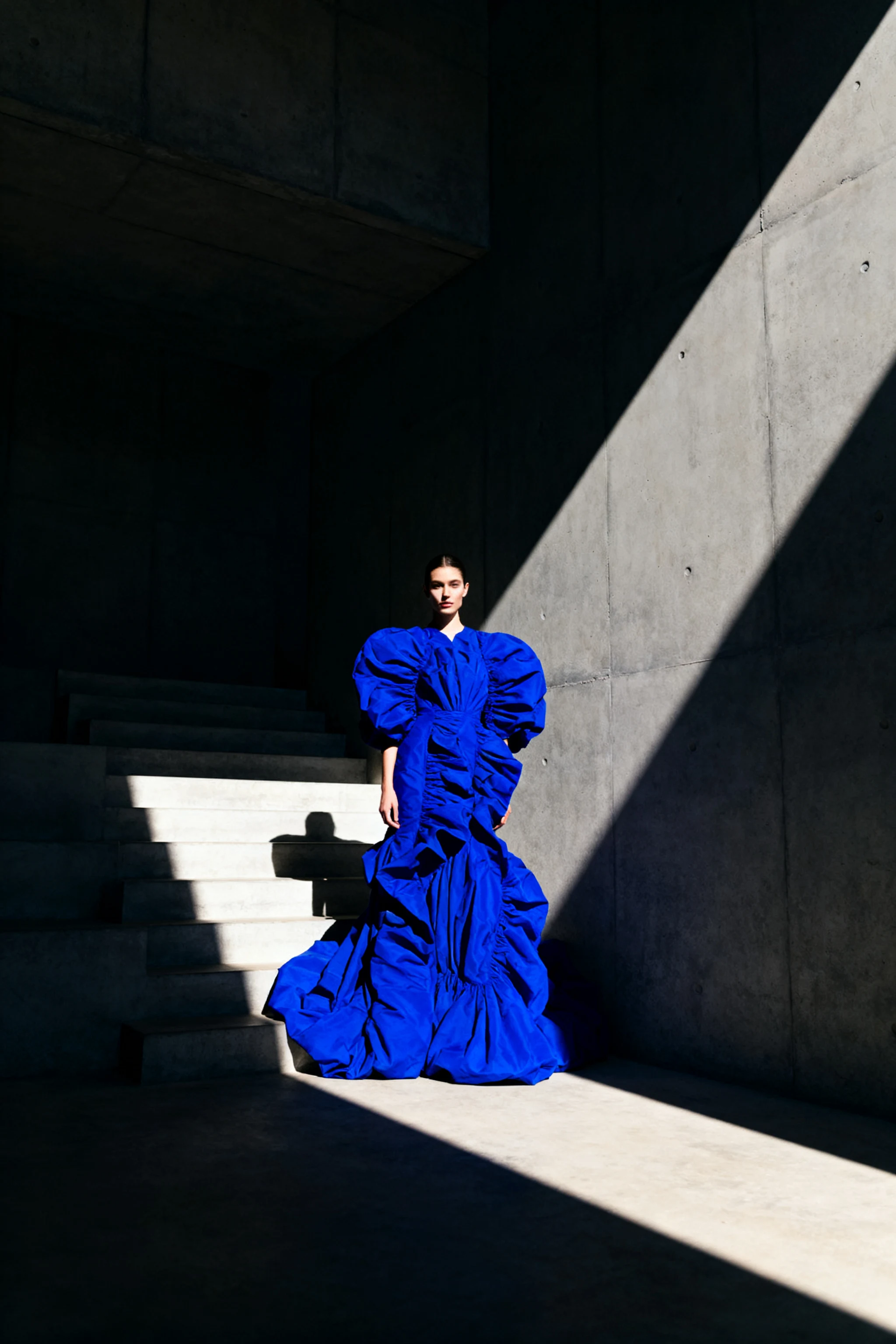 AI-generated fashion editorial photo of a model in a cobalt gown in a concrete stairwell, created with Seedream V4 on RenderFlow AI